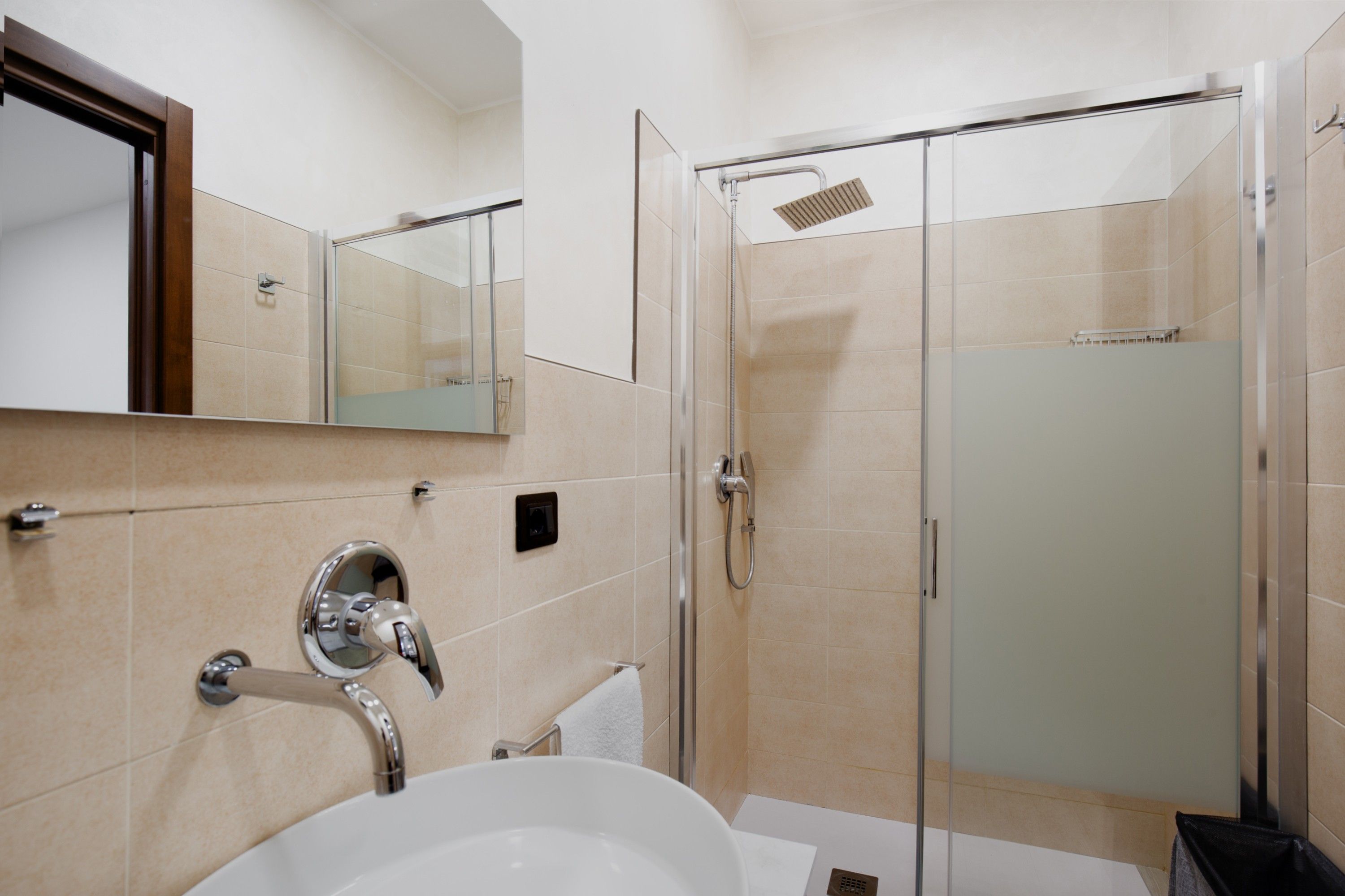 Ein modernes Badezimmer mit einer gläsernen Dusche, einem Waschbecken mit Chromarmatur und einem Spiegel darüber.