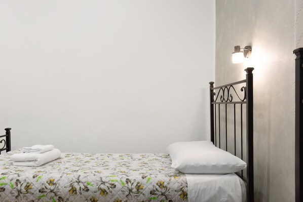 Una cama individual con una colcha de estampado floral, un almohadón blanco y una toalla blanca doblada al lado.