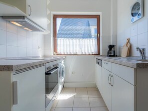 A compact kitchen with a built-in oven, a washing machine, and a coffee maker. - Holiday Apartment With 2 Bedrooms (St. Peter-Ording)