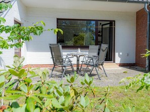 An outdoor patio with a table and chairs, a sliding glass door, and a white brick wall. - Holiday Apartment With 2 Bedrooms (St. Peter-Ording)