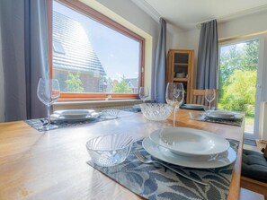 A dining table set with plates, bowls, and wine glasses, with a view of a building and greenery outside. - Holiday Apartment With 2 Bedrooms (St. Peter-Ording)