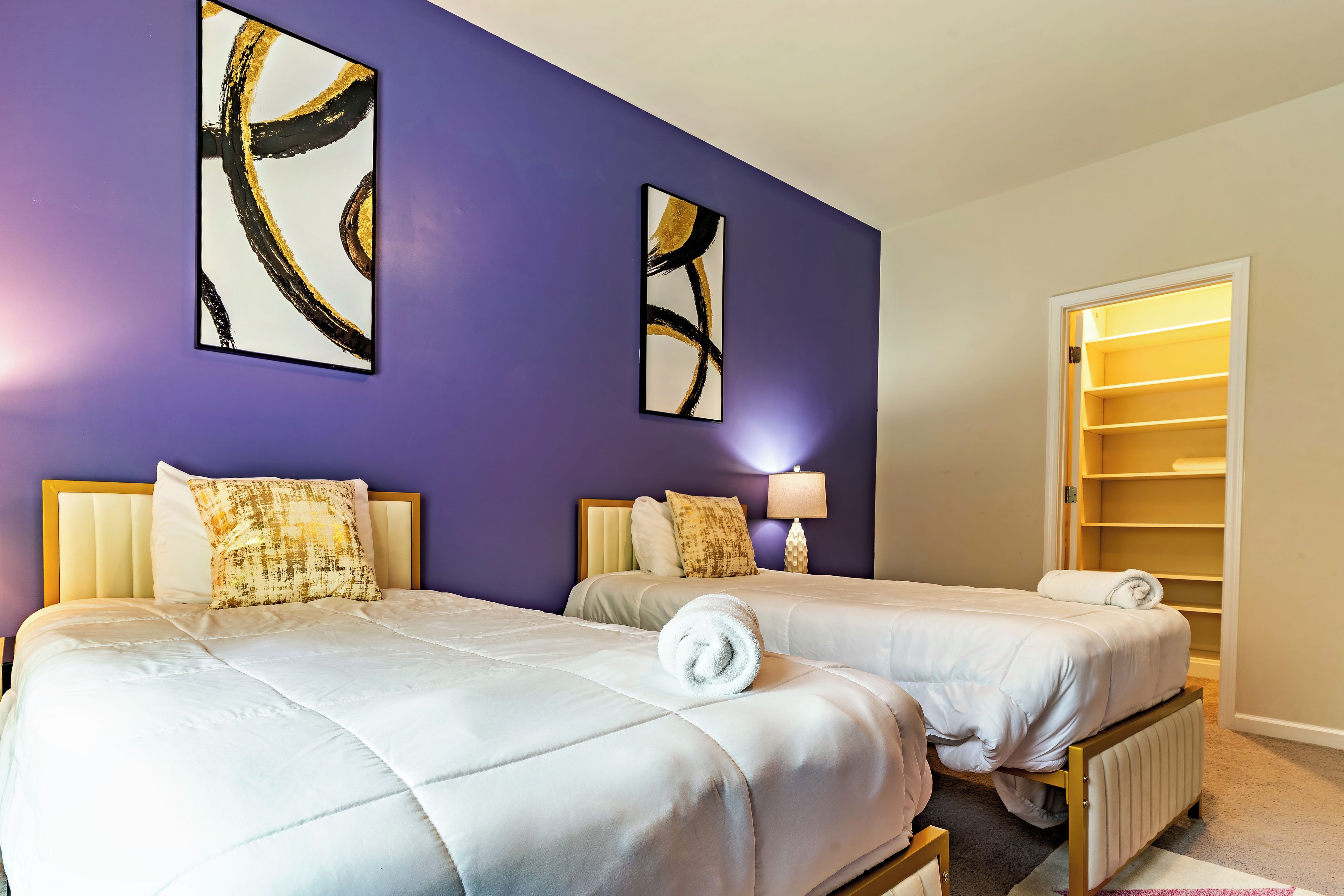 Habitación de hotel con dos camas, paredes moradas y arte abstracto.