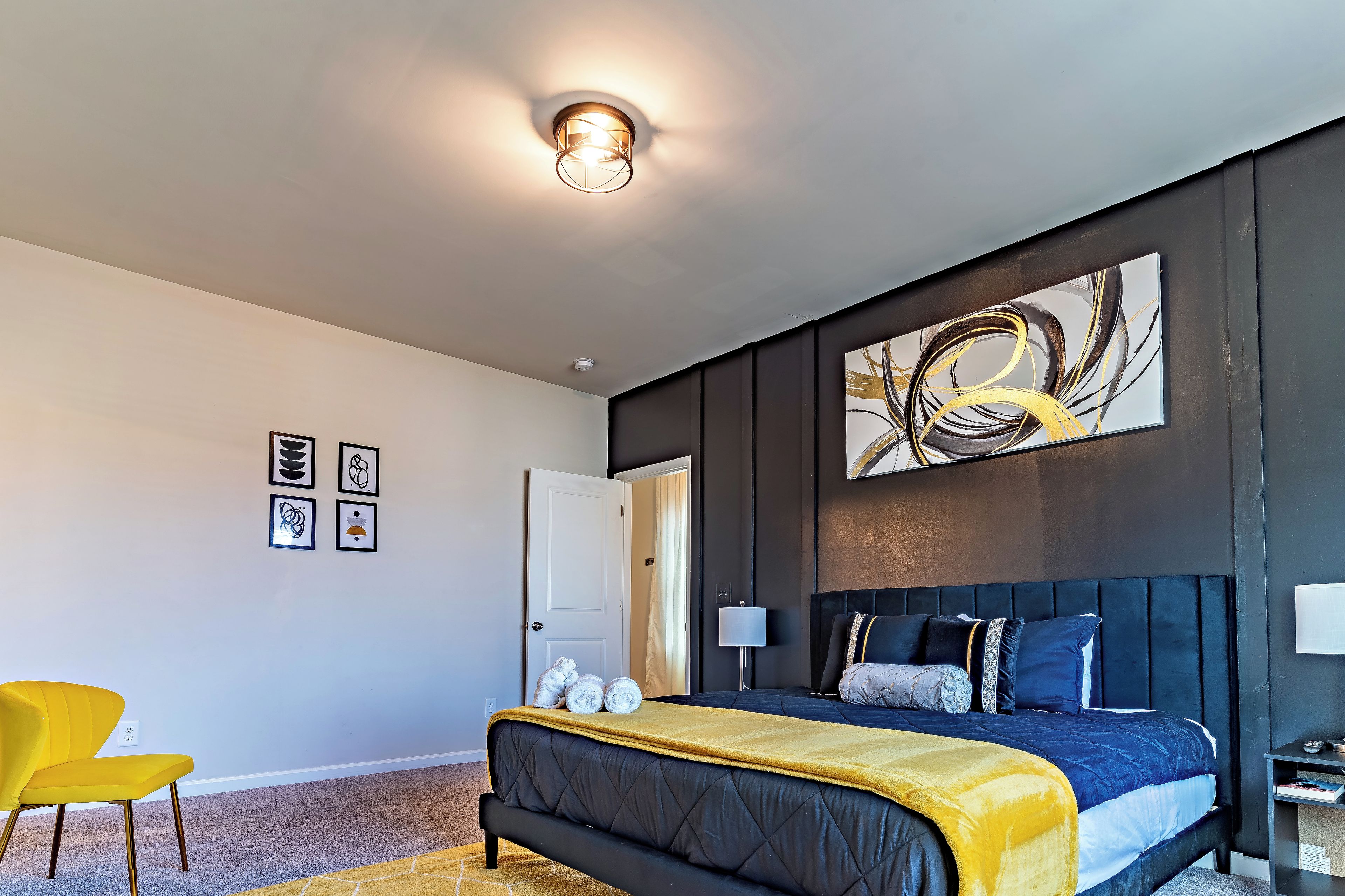 A modern bedroom with a large bed, a yellow chair, and a wall with abstract art.