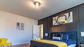 A modern bedroom with a large bed, a yellow chair, and a wall with abstract art.