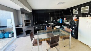 A modern kitchen with a glass dining table, black tiled backsplash, and stainless steel appliances. - Perfect com piscina e 3-bedroom house in Peruíbe for a relaxing getaway (Peruíbe)