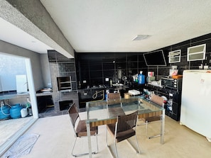A modern kitchen with a glass dining table, black tiled backsplash, and stainless steel appliances. - Perfect com piscina e 3-bedroom house in Peruíbe for a relaxing getaway (Peruíbe)