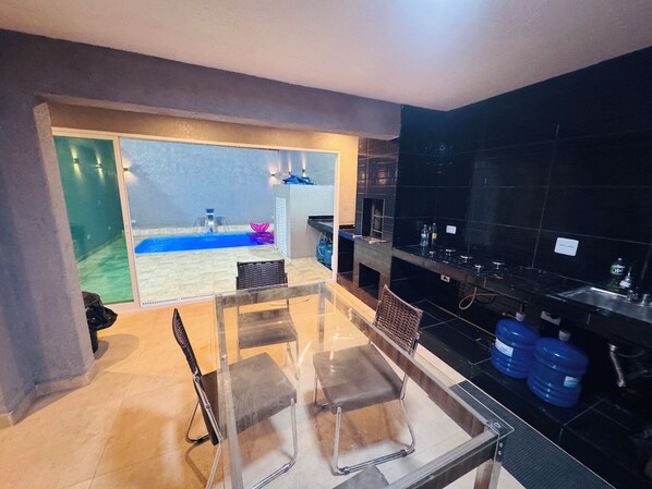 A modern kitchen with black tiled walls, a glass dining area, and a view of a swimming pool.