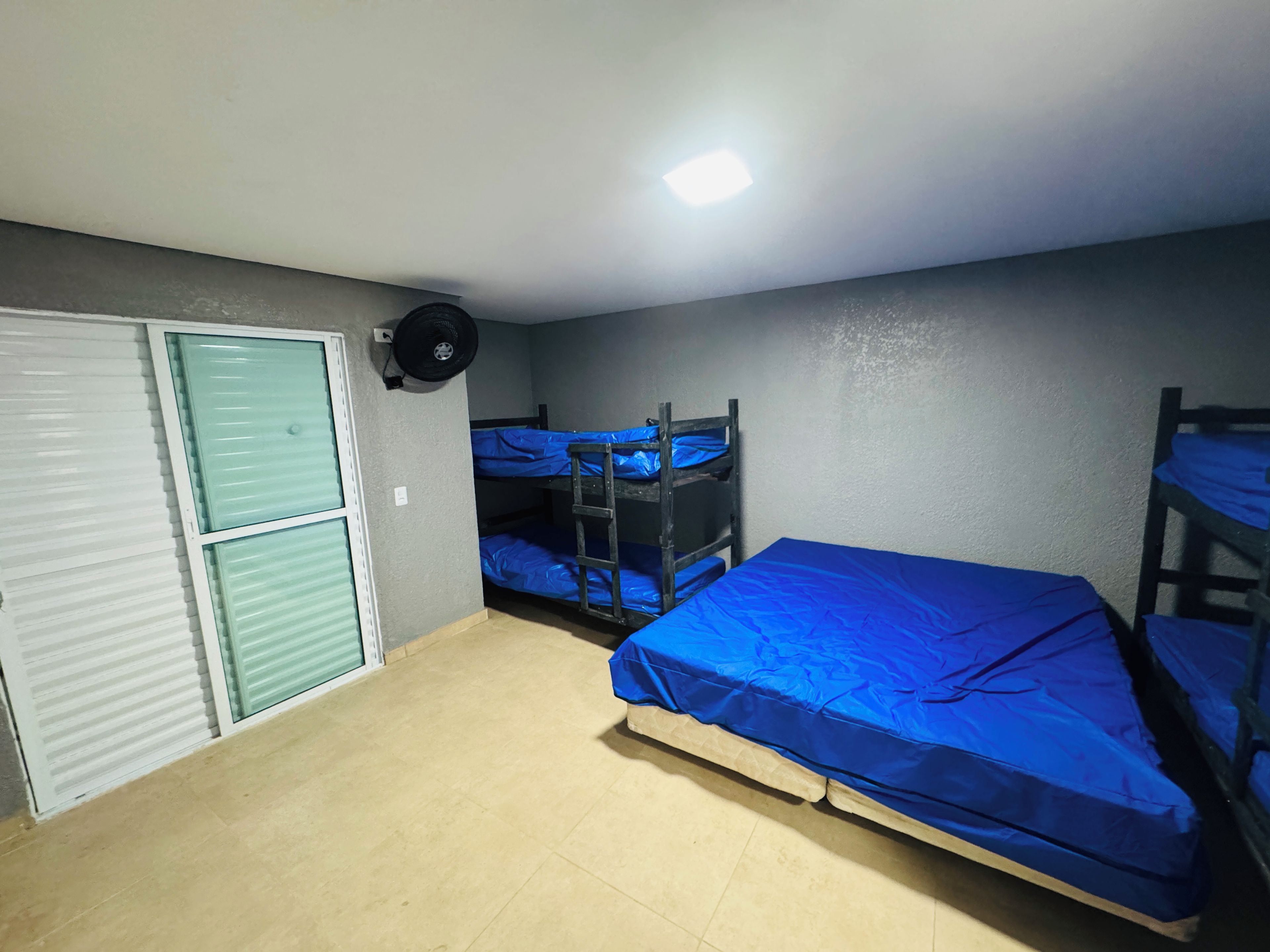 Quarto com beliches, porta fechada e ventilador de teto.