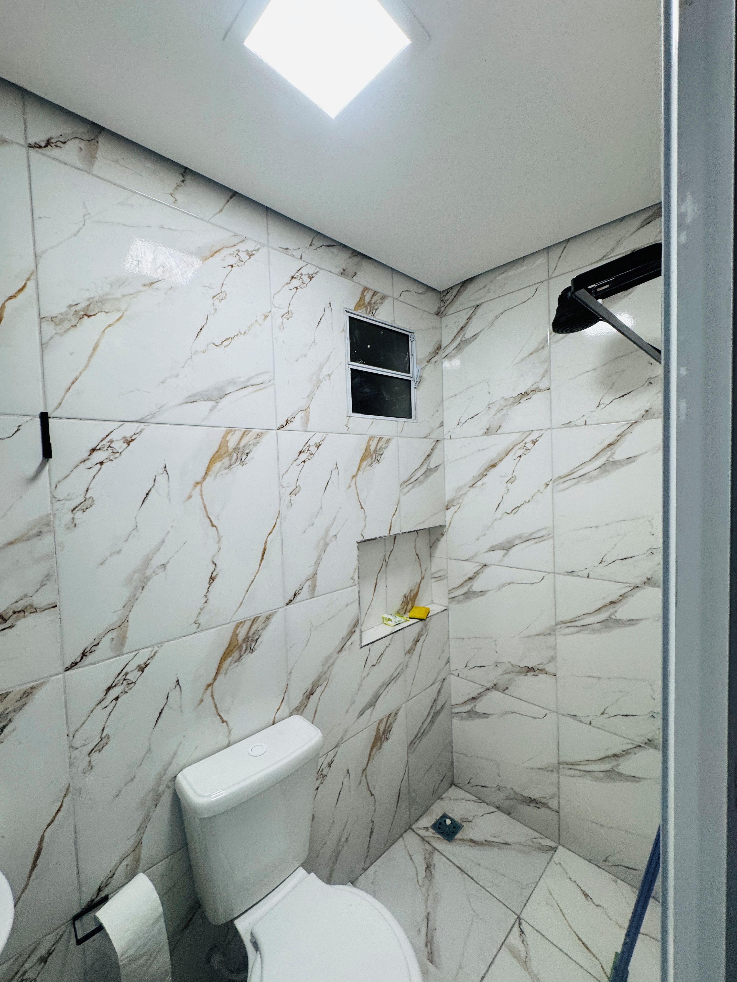 A bathroom with a toilet, a shower area, and a small window.