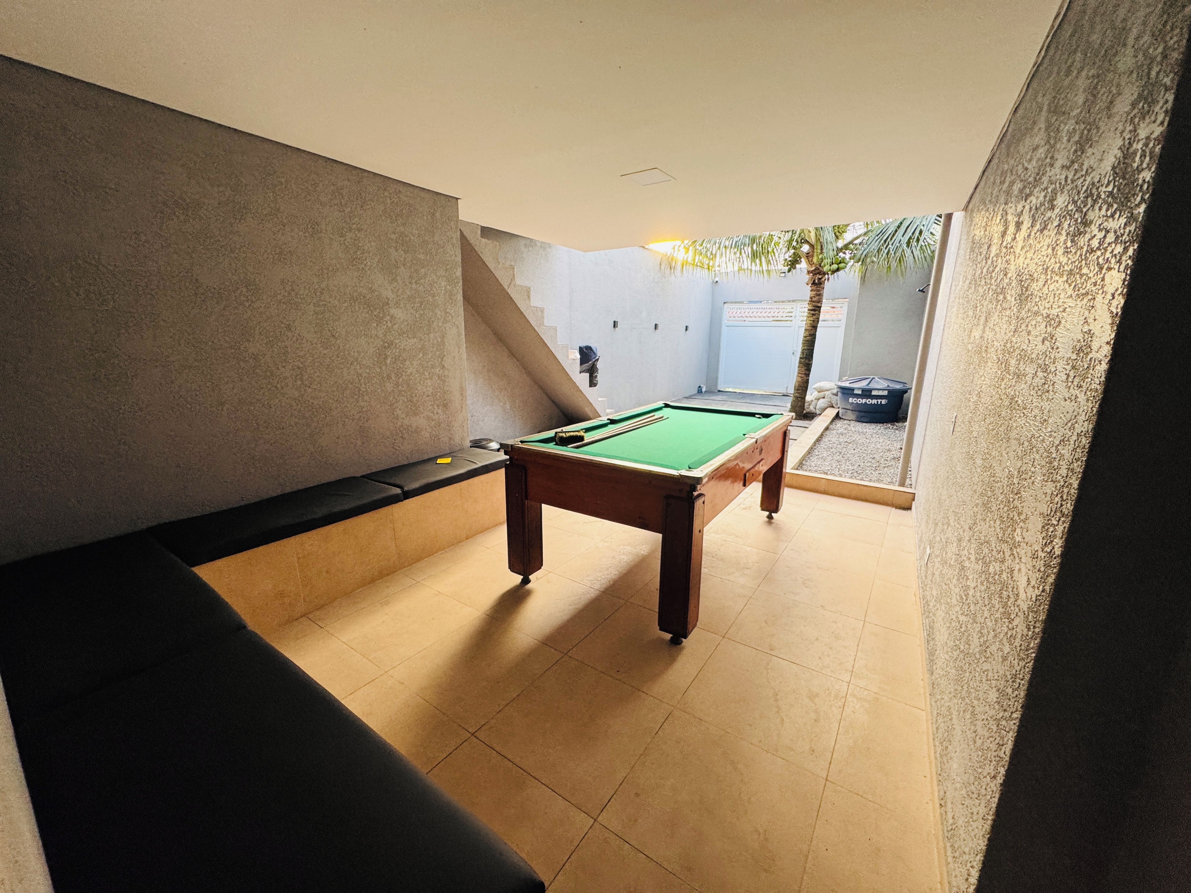 Mesa de bilhar em um ambiente com um banco e uma porta que dá para o exterior.