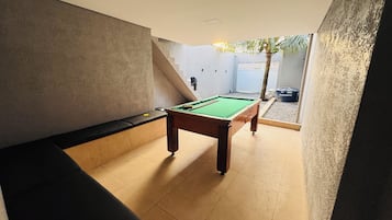 Mesa de bilhar em um ambiente com um banco e uma porta que dá para o exterior.