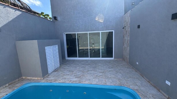 A swimming pool with a tiled deck, a sliding glass door, and a grey wall. - Perfect com piscina e 3-bedroom house in Peruíbe for a relaxing getaway (Peruíbe)