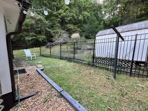 Ein umzäunter Garten mit einem weißen Gartenhaus, einem weißen Stuhl und einem Gartenbeet mit Mulch und Pflanzen.