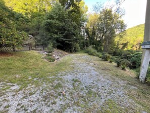 Ein Kiesweg führt durch eine Rasenfläche mit Bäumen und einem Holzzaun.