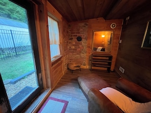 Ein gemütliches Blockhaus-Interieur mit einer hölzernen Bank, einer Steinwand und einem Fenster mit Blick auf einen umzäunten Garten.