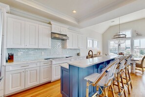 A spacious kitchen with white cabinetry, a blue island, and a bar area with wicker chairs. - Stunning Intracoastal Views + Sunset Porch | Easy Beach Access | 5BR | Sleeps 12 (Wrightsville Beach)