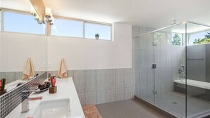 A modern bathroom with a glass-enclosed shower, a large vanity with a sink, and a window providing natural light.