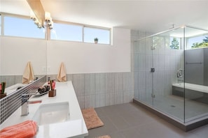 A modern bathroom with a glass-enclosed shower, a large vanity with a sink, and a window providing natural light. - Magnolia View Retreat | Rooftop Deck + Parking (Seattle)