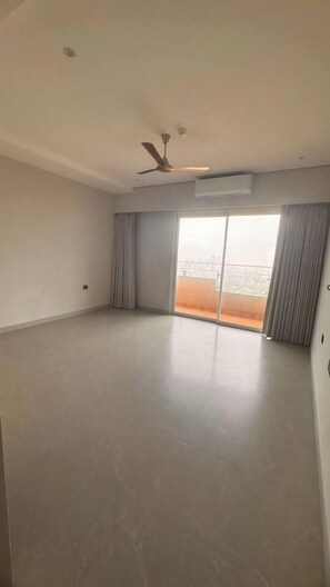 A spacious room with a large sliding glass door leading to a balcony, a ceiling fan, and a flat floor.