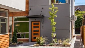 A modern two-story building with a flat roof, large windows, and a small garden area with a single tree.