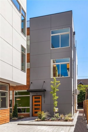 A modern two-story building with a flat roof, large windows, and a small garden area with a single tree. - Magnolia View Retreat | Rooftop Deck + Parking (Seattle)