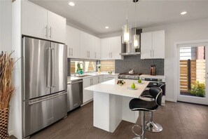 A modern kitchen with stainless steel appliances, white cabinetry, and a central island with bar stools.
