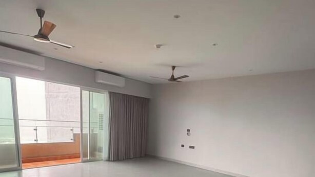 A spacious room with a large open area, a ceiling fan, and a sliding glass door leading to an outdoor balcony.