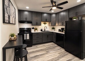 A modern kitchen with dark cabinets, a black refrigerator, and a ceiling fan. - The Hidden Gem : A Bold 4BR Home w/ Game Room + Movie Lounge (St. Louis)