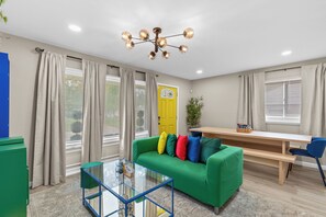 A modern living room with a green sofa, a glass coffee table, and a wooden dining table. - The Hidden Gem : A Bold 4BR Home w/ Game Room + Movie Lounge (St. Louis)