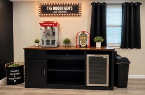 A snack bar with a popcorn machine, a mini fridge, and a trash bin. - The Hidden Gem : A Bold 4BR Home w/ Game Room + Movie Lounge (St. Louis)