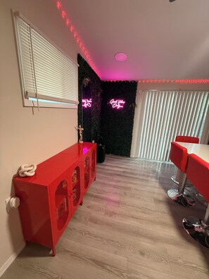 A room with a red cabinet, a black wall with neon signs, and a window with blinds. - The Hidden Gem : A Bold 4BR Home w/ Game Room + Movie Lounge (St. Louis)