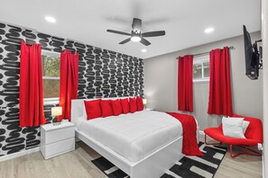 Ein modernes Schlafzimmer mit einem weißen Bett, roten Vorhängen, einem roten Sessel und einer schwarz-weißen Wand.