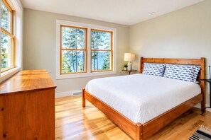 Un dormitorio con una cama de madera, una mesita de noche con una lámpara y una ventana con vistas a árboles y agua.