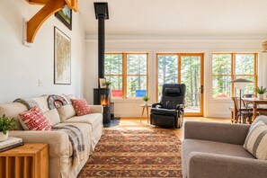 A cozy living room with a fireplace, a sofa, a recliner, and a dining area with large windows.