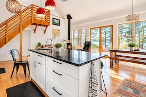 Una cocina moderna con una isla central, una escalera de madera y grandes ventanales que ofrecen vistas al exterior.