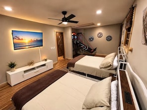 Une chambre avec deux lits, un ventilateur de plafond, un téléviseur fixé au mur et un panier de basket.