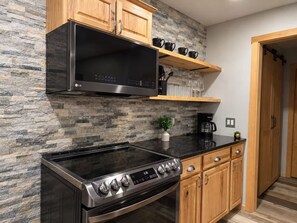 A modern kitchen with a stone backsplash, wooden cabinets, a black microwave, and a stainless steel stove. - Enjoyable 3-bedroom house with AC in charming Nashville (Nashville)