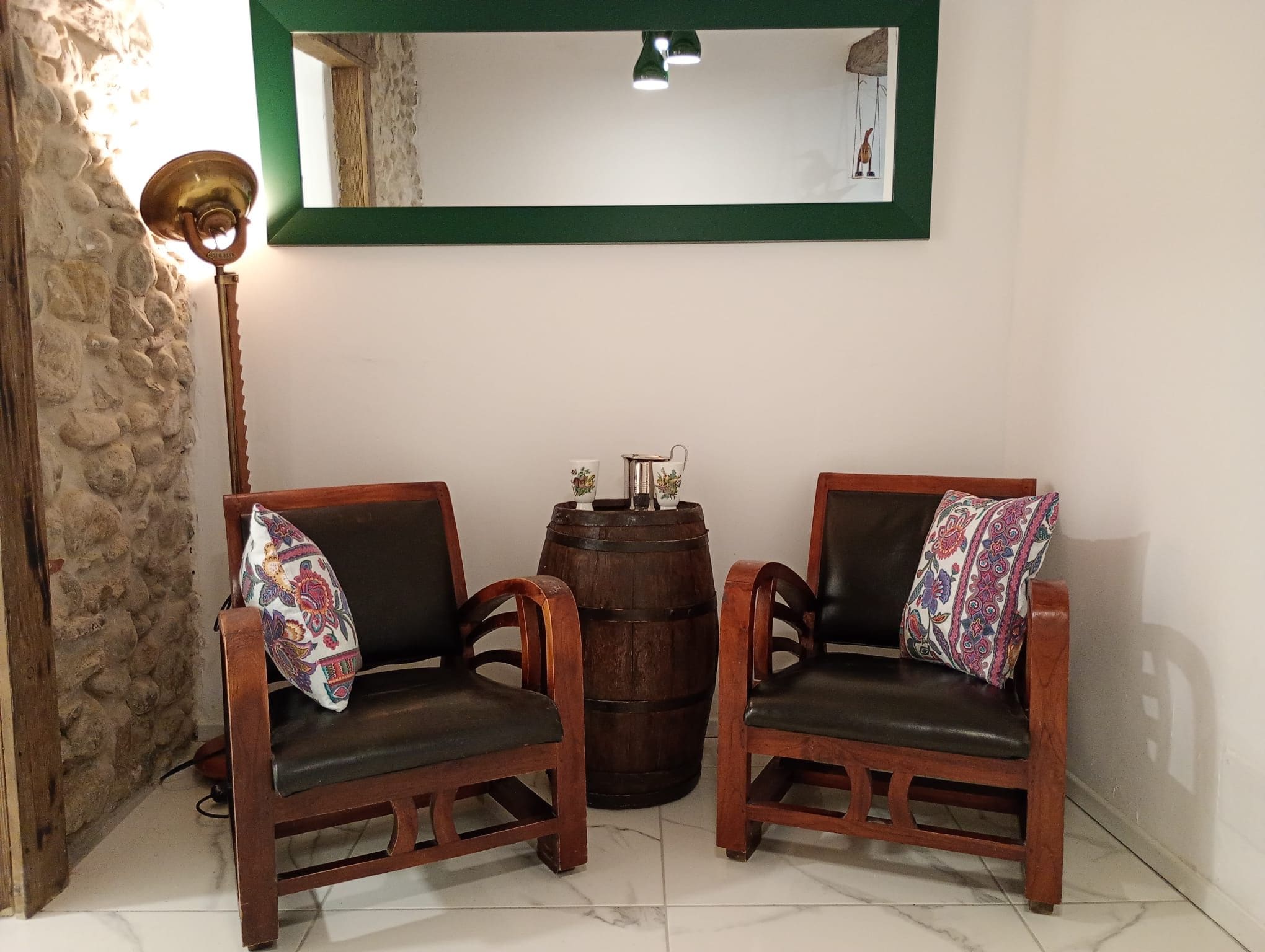 Deux chaises en bois avec des coussins à motifs, un tonneau en bois et un lampadaire.