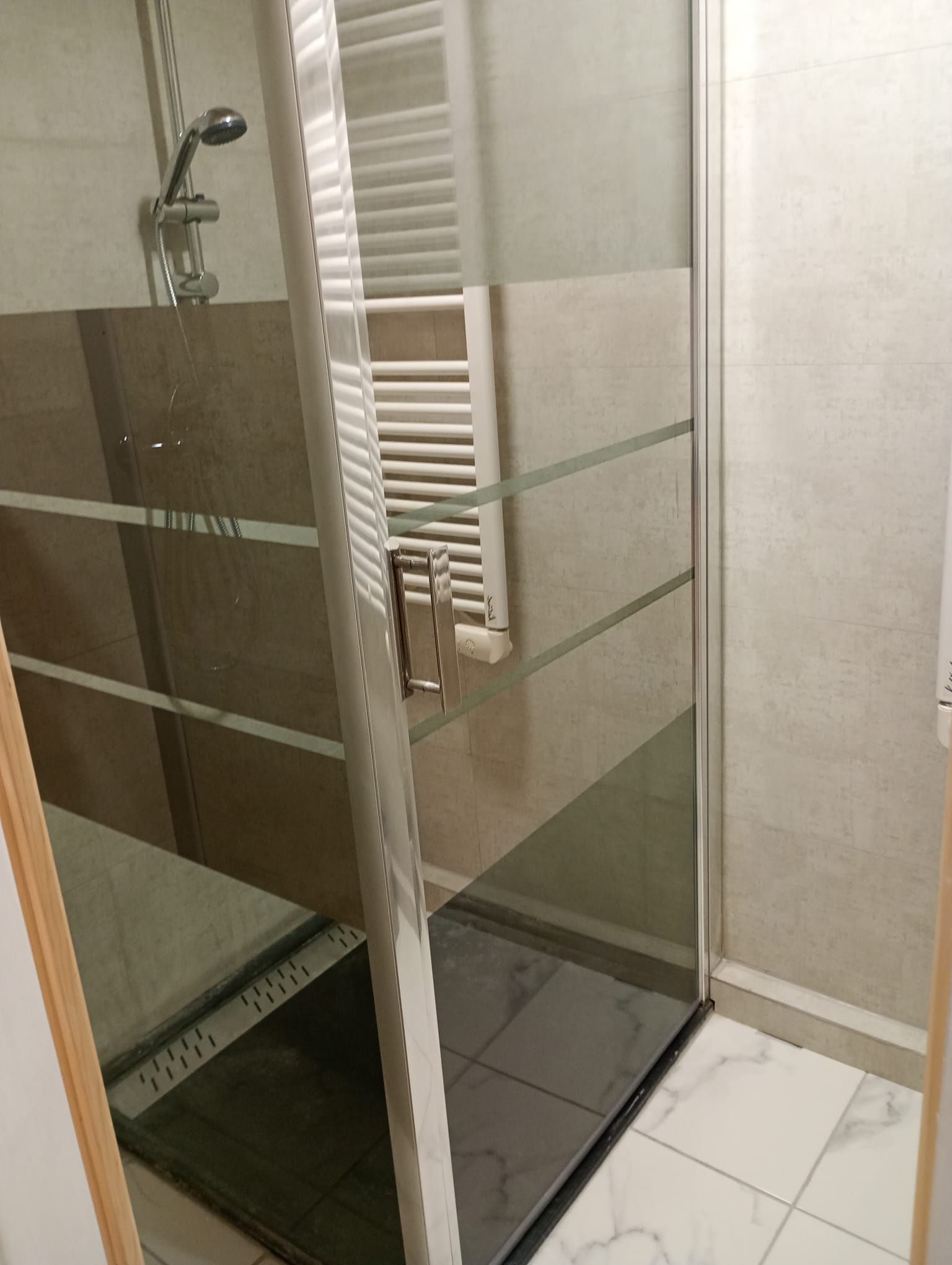 A glass-enclosed shower area with a white tiled floor and a glass door.
