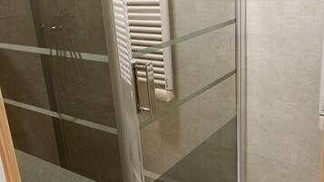 A glass-enclosed shower area with a white tiled floor and a glass door.
