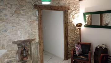 Habitació rústica amb parets de pedra, una porta de fusta, una làmpada penjant verda, un fanal tradicional, una cadira de pell i un barril de fusta.