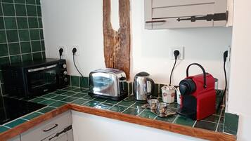 Et køkken med en brødrister, elkedel og kaffemaskine på bordet, en mikrobølgeovn og en vask med træbordplade.