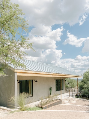 A modern house with a sloped metal roof, large windows, and a landscaped garden with a cactus. - Hill Country Oasis: 8‑Bedroom Resort with Pool, Scenic Views & Gathering Spaces (Dripping Springs)