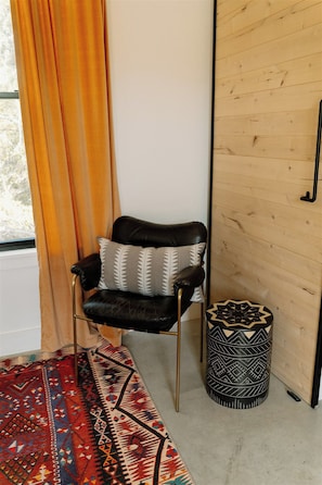 A room with a black leather chair, patterned cushions, a patterned rug, a wooden wall, and a decorative stool. - Hill Country Oasis: 8‑Bedroom Resort with Pool, Scenic Views & Gathering Spaces (Dripping Springs)