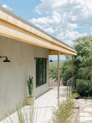 A modern building with a covered patio, large windows, and a view of the landscape. - Hill Country Oasis: 8‑Bedroom Resort with Pool, Scenic Views & Gathering Spaces (Dripping Springs)