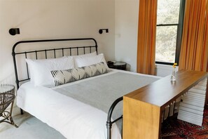 A bed with a metal frame, white bedding, and a wooden bedside table. - Hill Country Oasis: 8‑Bedroom Resort with Pool, Scenic Views & Gathering Spaces (Dripping Springs)