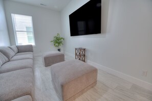 A modern living room with a sectional sofa, a small table, and a potted plant. - BRAND NEW ACROSS FROM OCEAN 12 beds/10 baths • Pvt Pool and Spa • Sleeps 28 (North Myrtle Beach)
