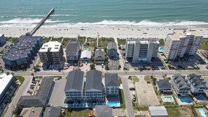 An aerial view of a coastal area with a beach, a pier, and various buildings including hotels and residential structures. - BRAND NEW ACROSS FROM OCEAN 12 beds/10 baths • Pvt Pool and Spa • Sleeps 28 (North Myrtle Beach)