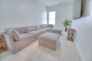 Ein modernes Wohnzimmer mit einem Ecksofa, einem Hocker, einem kleinen Holztisch und einem Blumentopf.