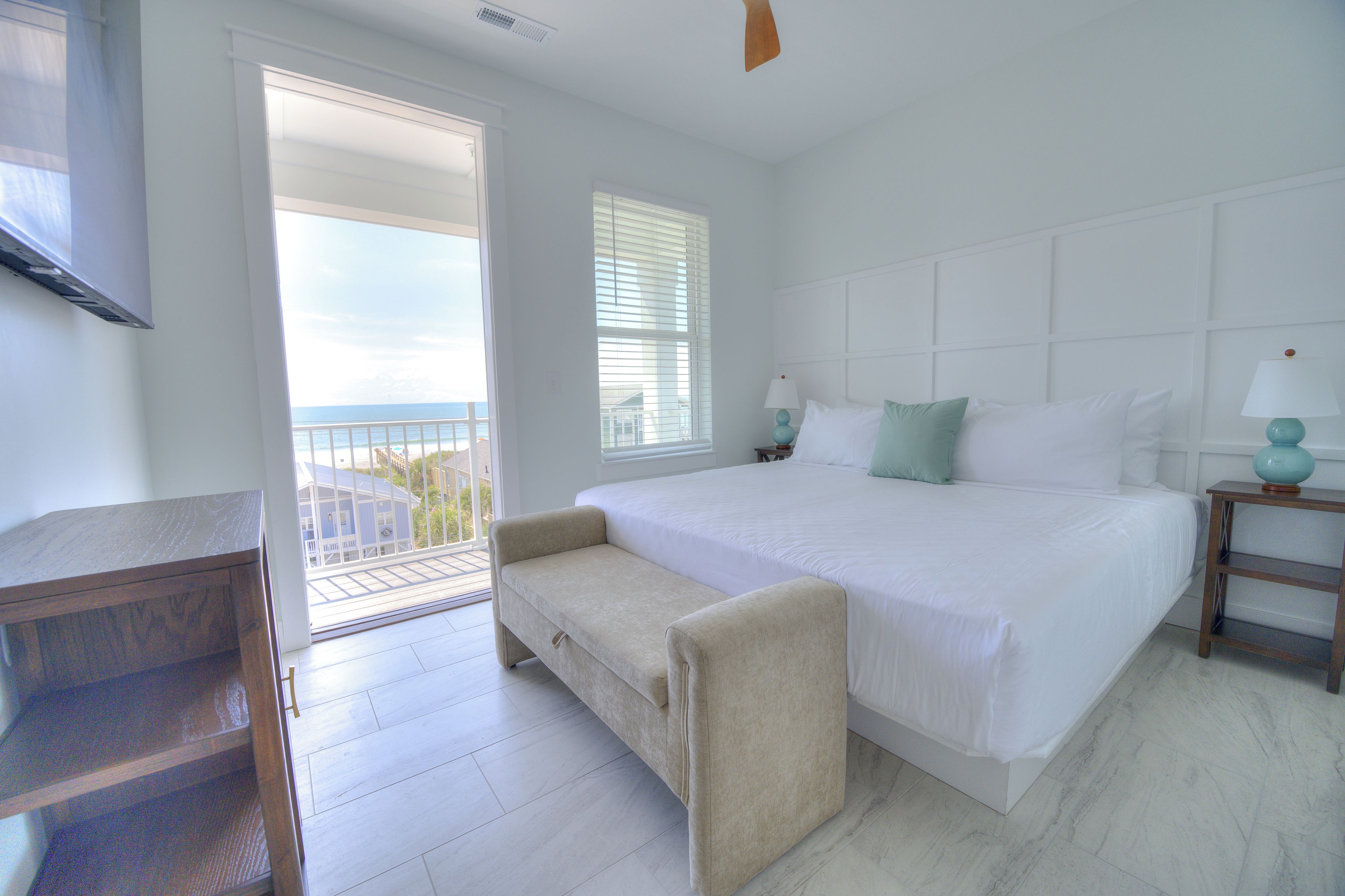 A bedroom with a large bed, a small sofa, a TV, and a balcony with a view.